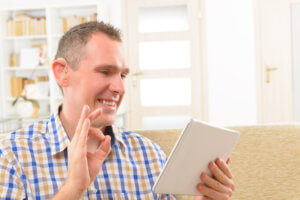 Man wearing hearing aids using iPad & signing